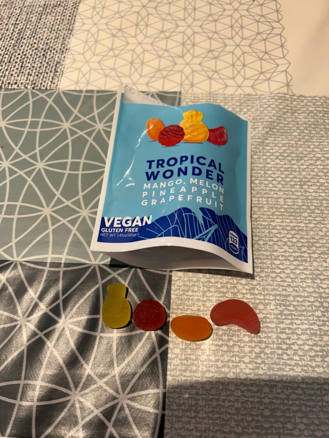 A packet of Jealous Sweets Tropical Wonder and 4 sweets lie on a tablecloth with various duck egg colour scheme patterns.