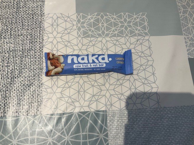 A Nakd Cashew Cookie bar lies on a tablecloth with various duck egg colour scheme patterns.