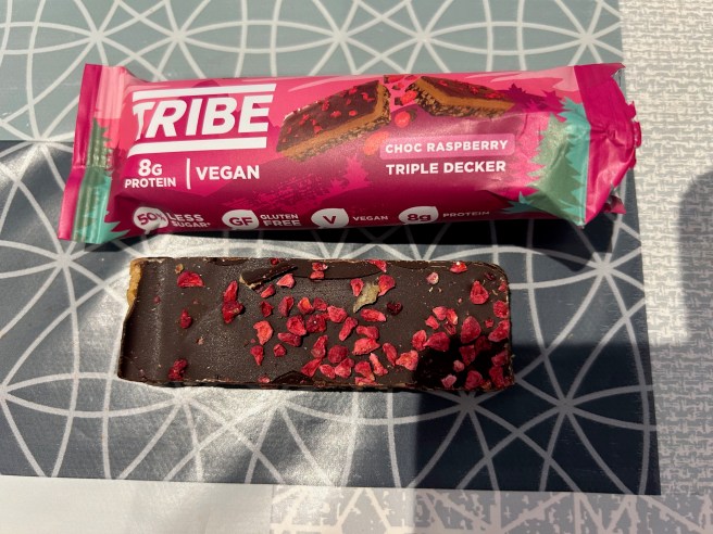 The empty Tribe Triple Decker wrapper and the top of the bar itself lie on a tablecloth with various duck egg colour scheme patterns.