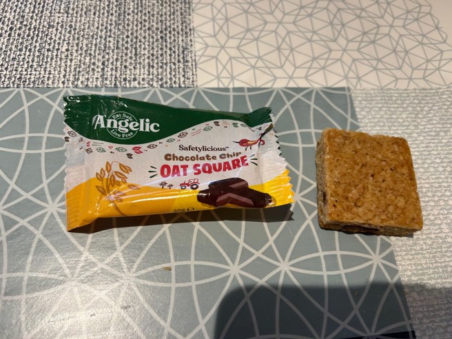 The wrapper for the Angelic Oat Square and the top of the square itself lie on a tablecloth with various duck egg colour scheme patterns.