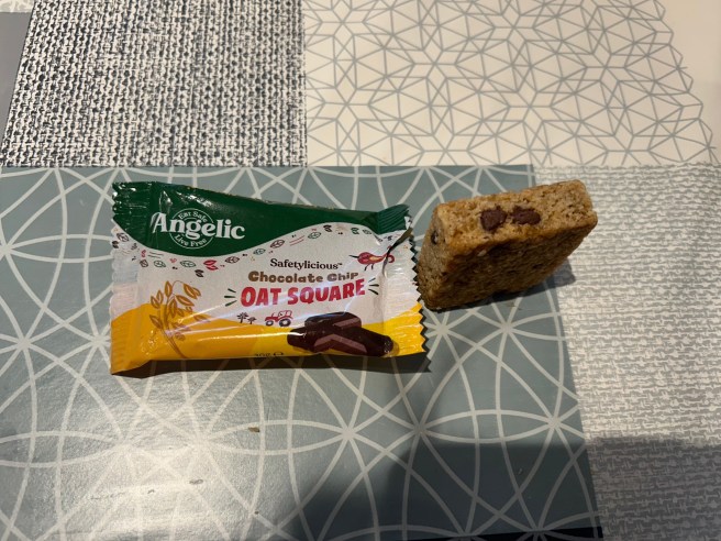 The empty Angelic Oat Square wrapper and the side of the square itself lie on a tablecloth with various duck egg colour scheme patterns.