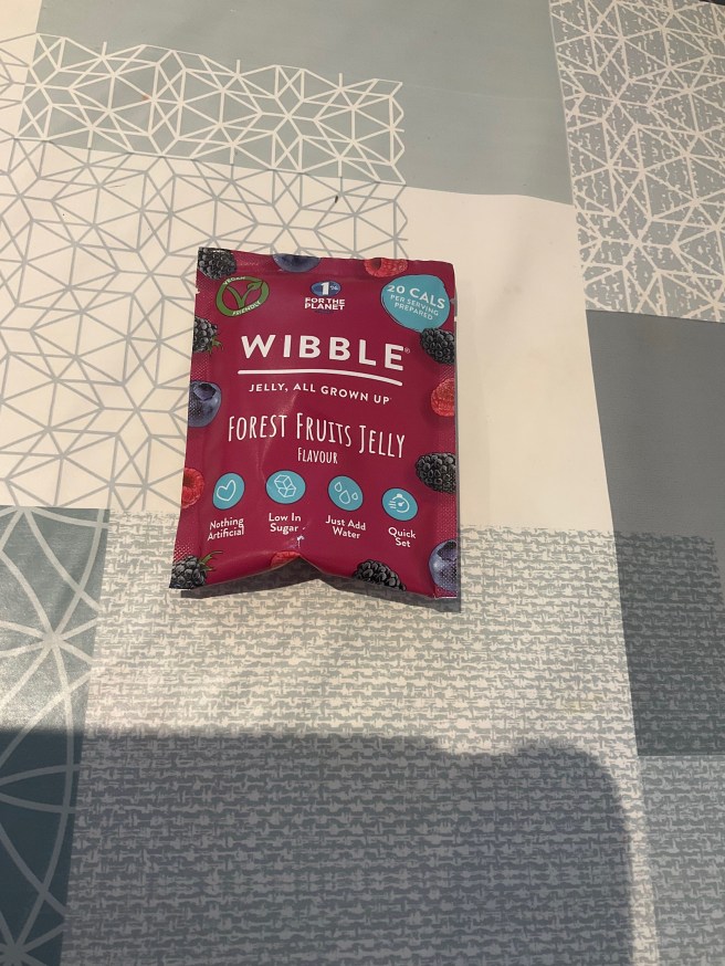 A Packet of Wibble Jelly lies on a tablecloth with various duck egg colour scheme patterns.
