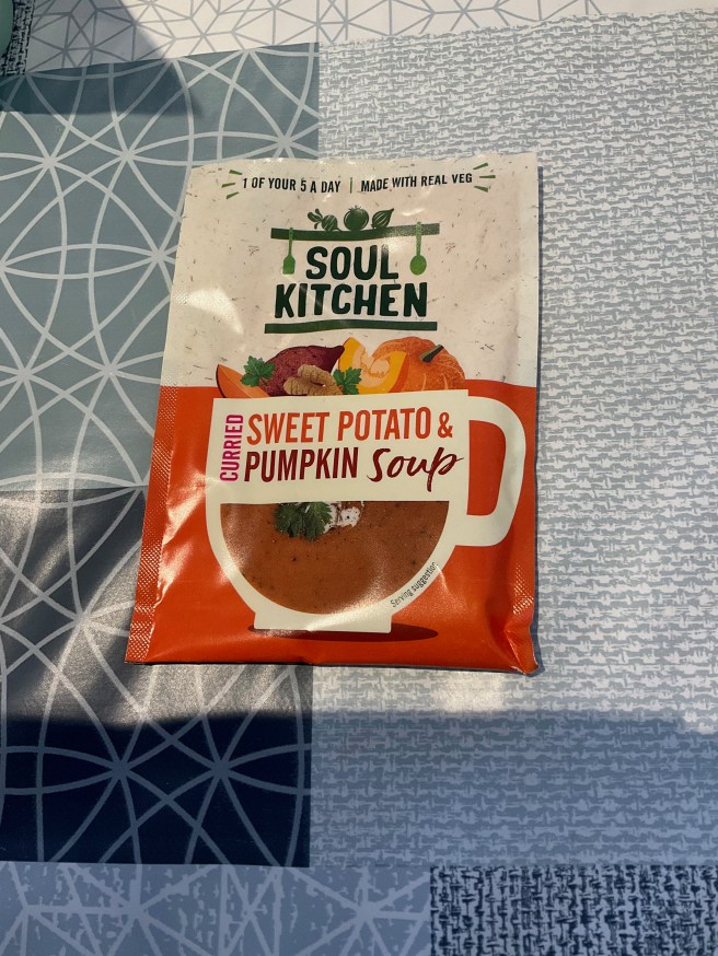 A packet of Soul Kitchen instant soup lies on a tablecloth with duck egg colour scheme patterns.