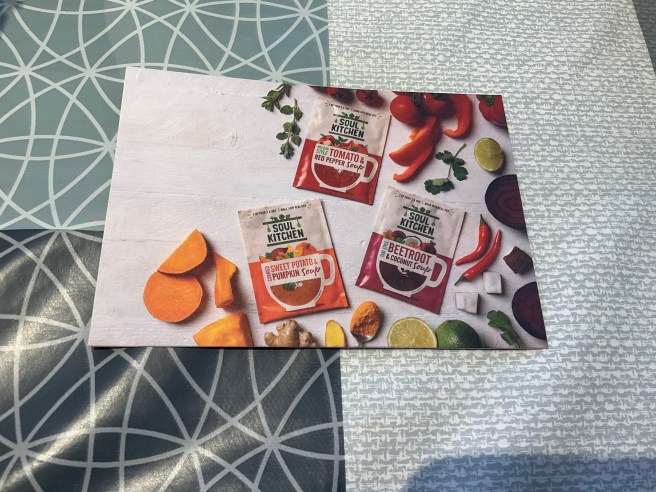 A Soul Kitchen flyer lies on a tablecloth with duck egg colour scheme patterns.