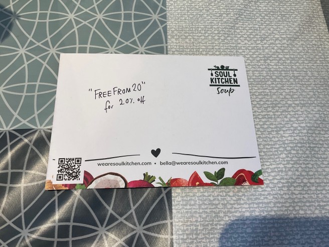 The back of a Soul Kitchen Leaflet lies on a tablecloth with a duck egg colour scheme pattern.