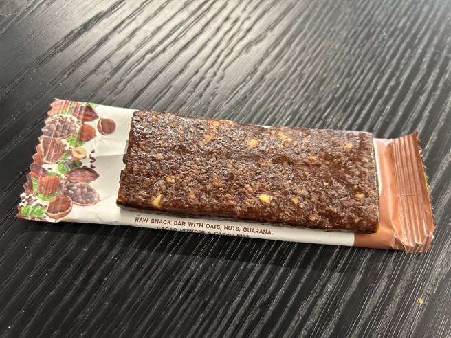 The Rheal Energy bar lies on top of its wrapper lies on a dark wooden tabletop.