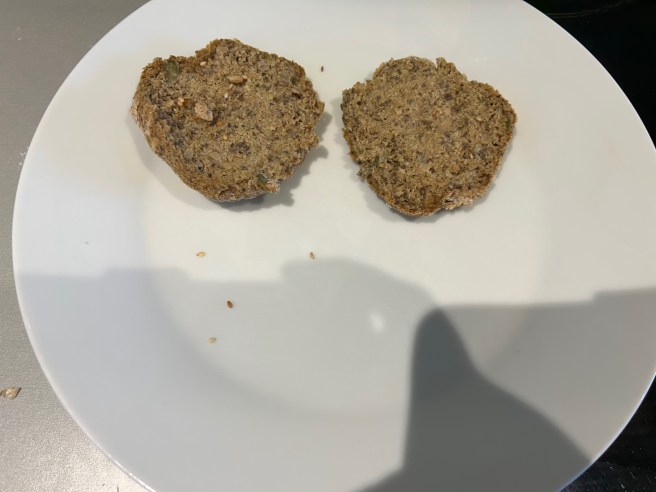 An open seeded bread roll lies on a white plate.
