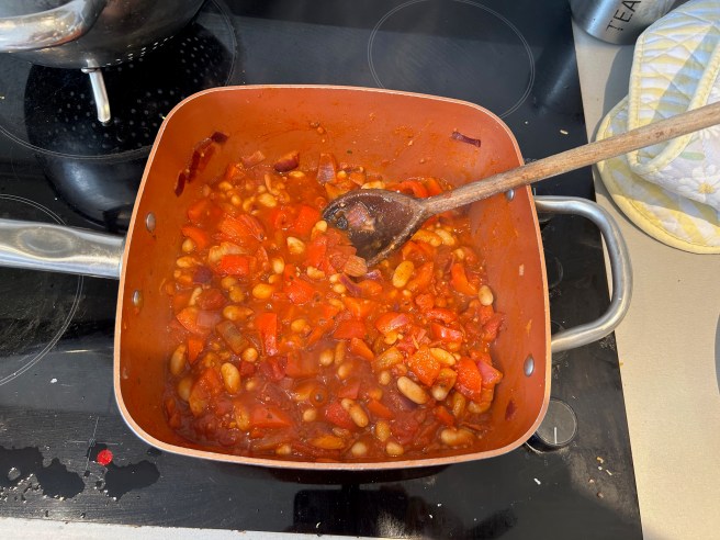 A large saucepan of vegetable chilli sits on an electric hob.