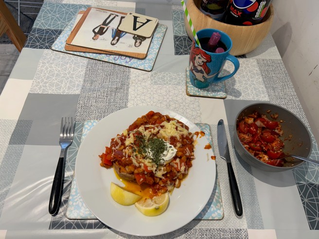 A plate of a Sweet Potato Jacket with Ketchup Chilli and a bowl of salsa sit on a tablecloth with duck egg colour scheme patterns.