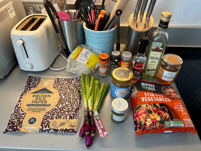Several ingredients for rice wrap spring rolls are arranged on a grey kitchen worktop.