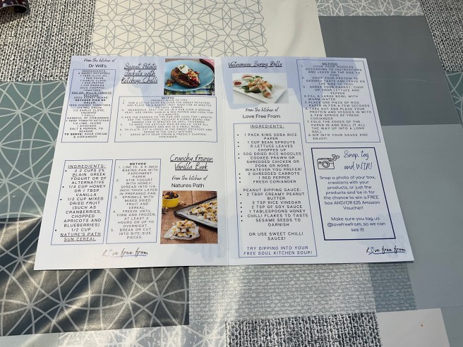 The open Love Free From April 2024 leaflet lies on a tablecloth with duck egg colour scheme patterns.